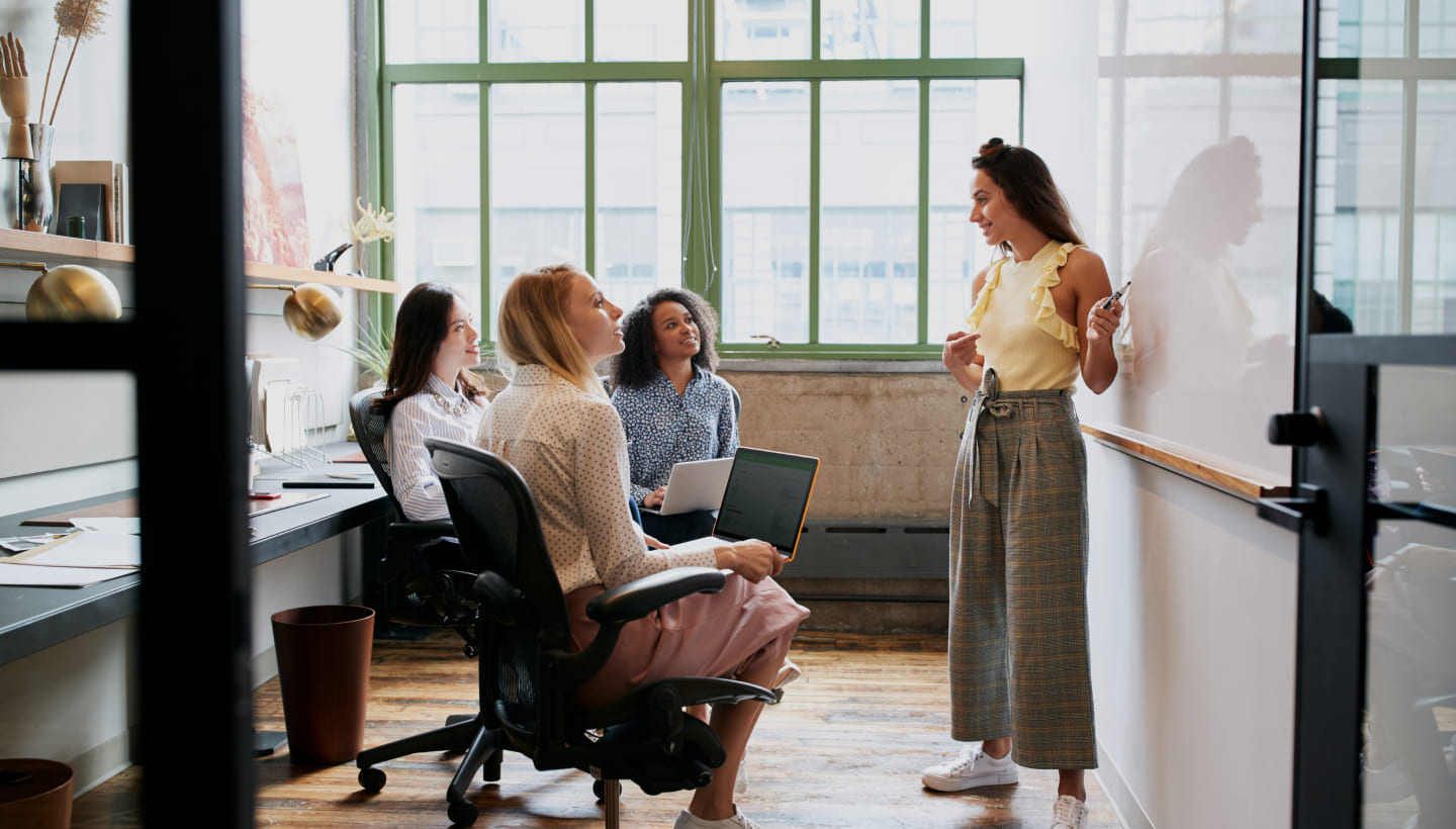 Kolleginnen im Einzelhandel halten Meeting zur Mitarbeiterengagement-Steigerung in Büro mit Whiteboard und den eigenen Laptops ab.