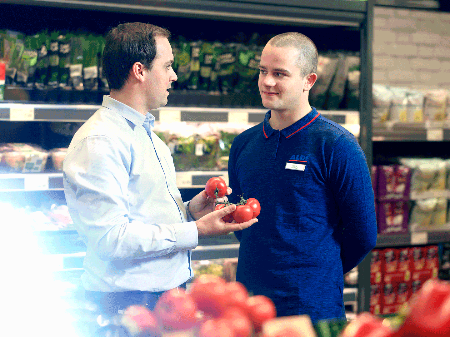 Zwei Supermarktangestellte sprechen miteinander im Gang einer Filiale über die Personalkosten.