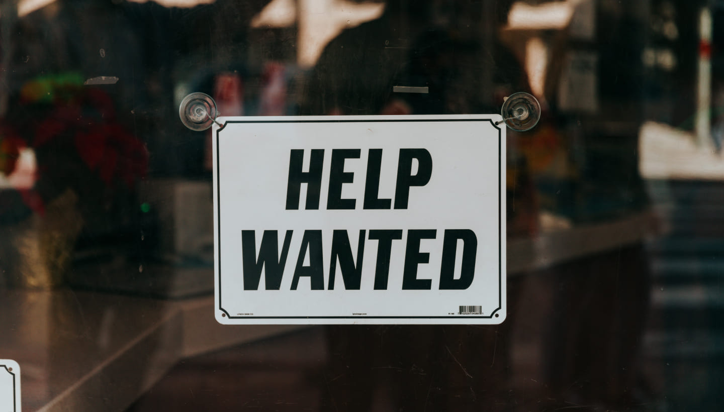 Ein Schild vor einem Einzelhandelsgeschäft auf dem 'Help Wanted'' steht.