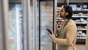 Männlicher Angestellter der mittels KI im Einzelhandel den Bestand in einer Supermarkt-Tiefkühltruhe mittles KI überprüft